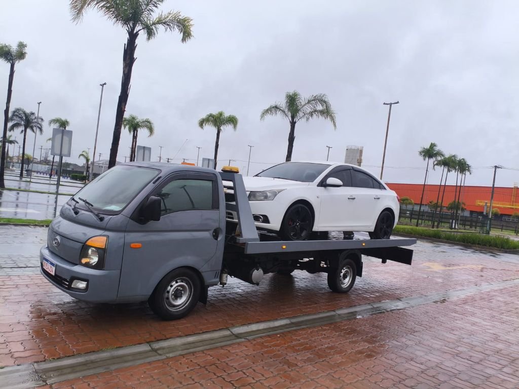 Carro sedan branco transportado em guincho plataforma